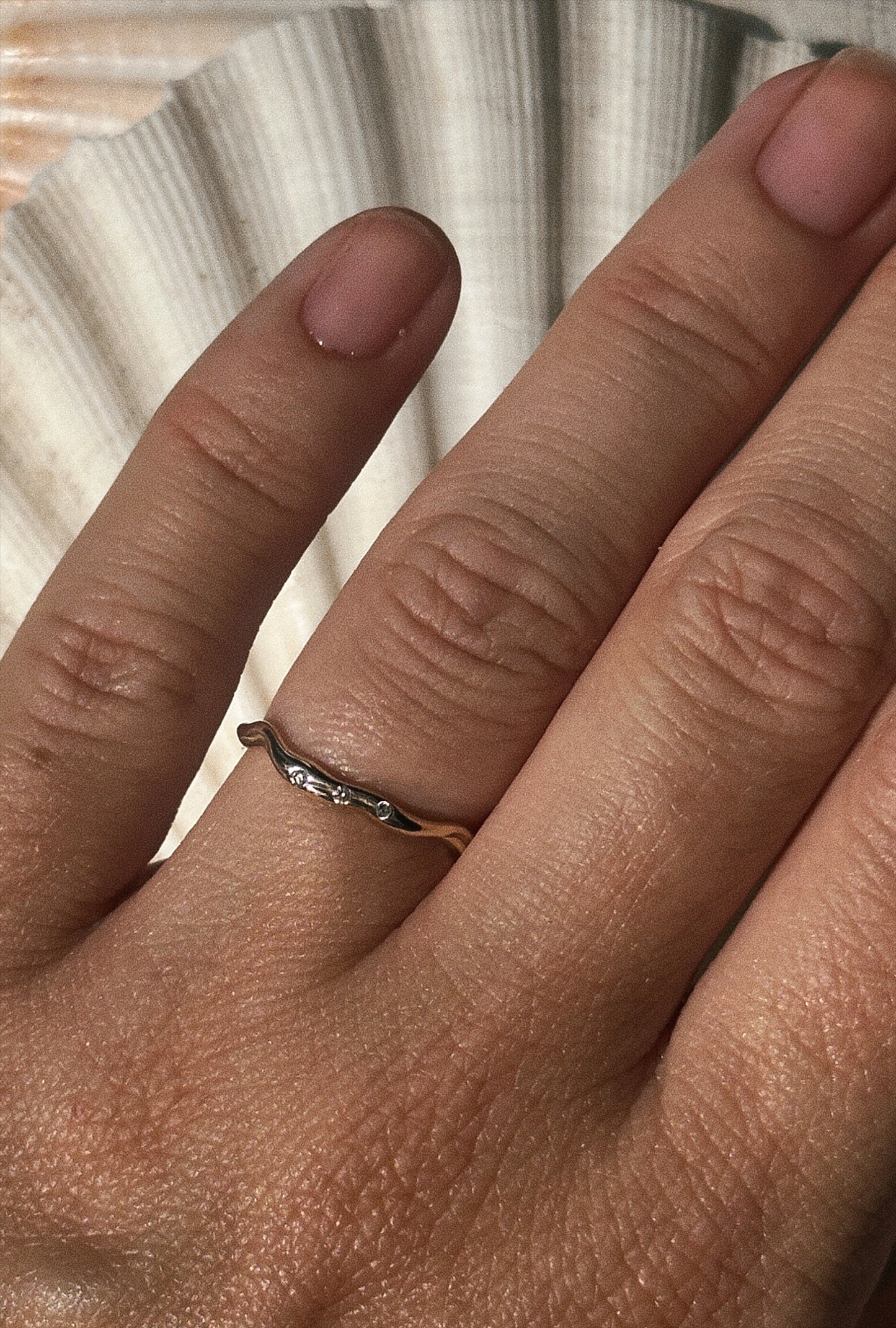 en hånd med en enkelt vielsesring i guld i organiske former ligger ovenpå en stor muslinge skal.