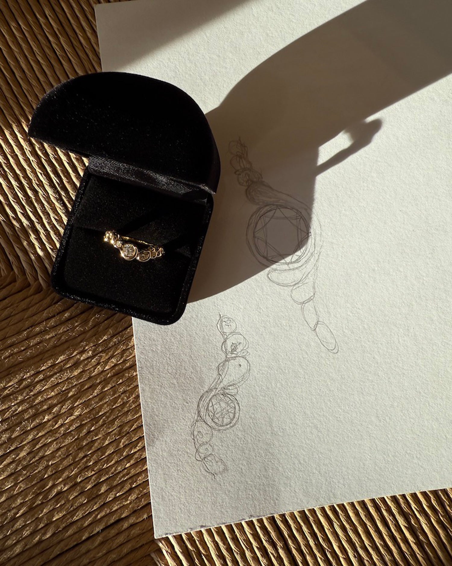 forlovelsesring i genanvendt guld med diamanter i sort æske. Æsken ligger ovenpå nogle håndtegnet design skitser der ligger ovenpå en wegner stol.
