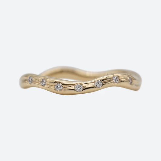 En ring i guld set forfra med syv diamanter på hvid baggrund. Ringen er formgivet organisk og bølger elegant.