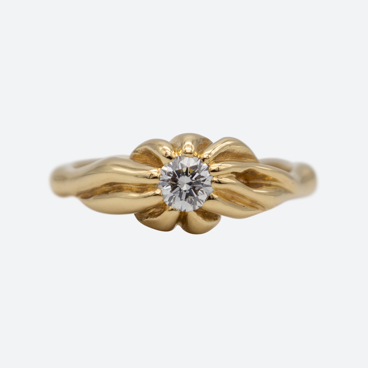 Ring set forfra i guld med stor diamant på hvid baggrund. Guldet er formgivet som rødder der mødes i midten hvor en stor brilliantslebet diamant er placeret i midten. Design af Michell Liljefelt