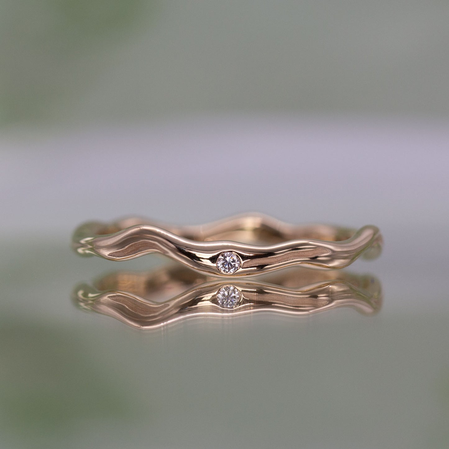 En tynd guld ring set forfra med en diamant. Formgivningen bugter sig i en harmonisk cirkel.
