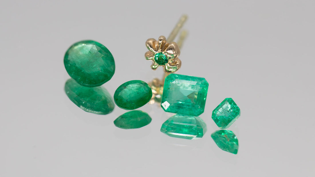 Fire smaragder ligger foran en guld ørering der også er fattet med en smaragd. De er i forskellige slib og størrelser, fra cushion cut til oval, dog er alle i en fortryllende grøn farve.  