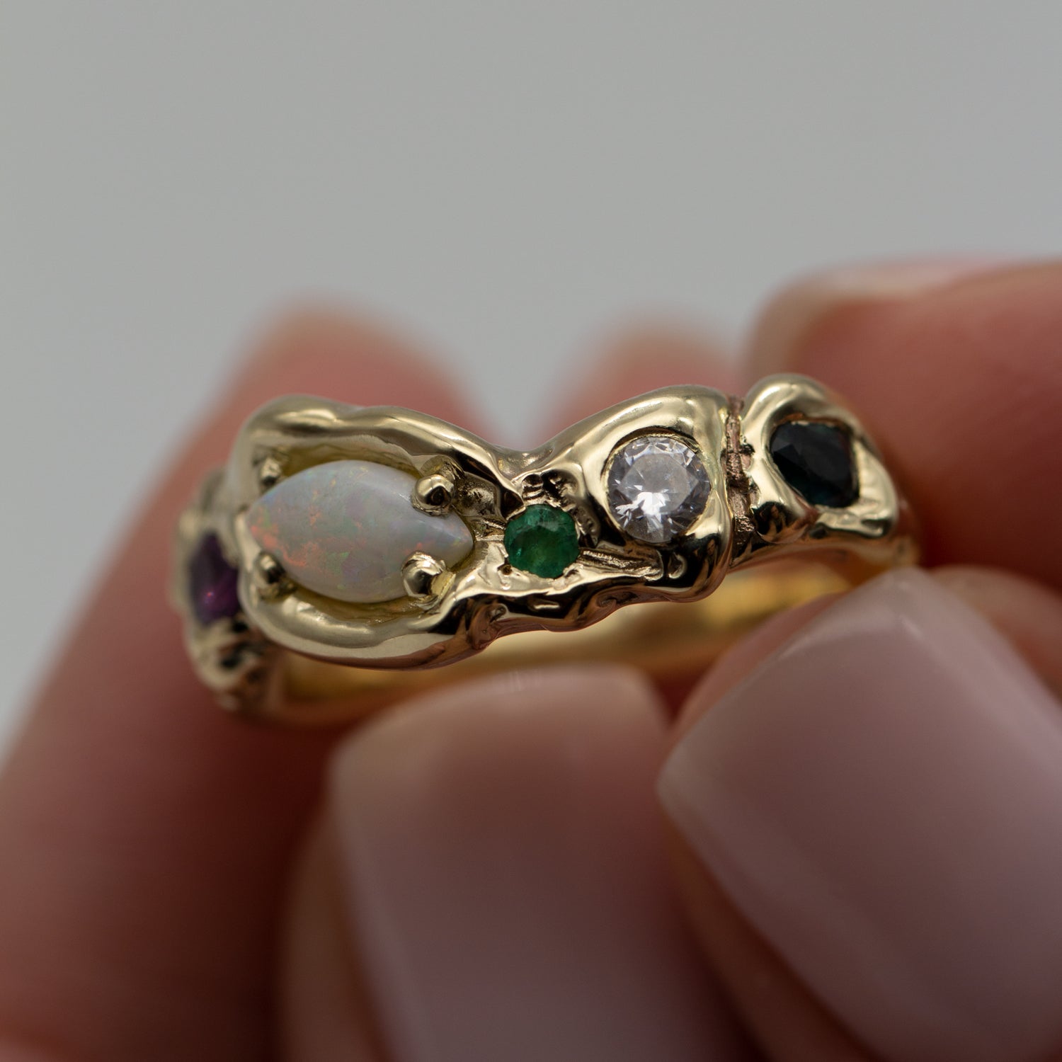 En unik formgivet ring i guld med Opal, diamant, smaragd, rubin holdes i fingerspidserne. En unika ring i genanvendt 14kt guld