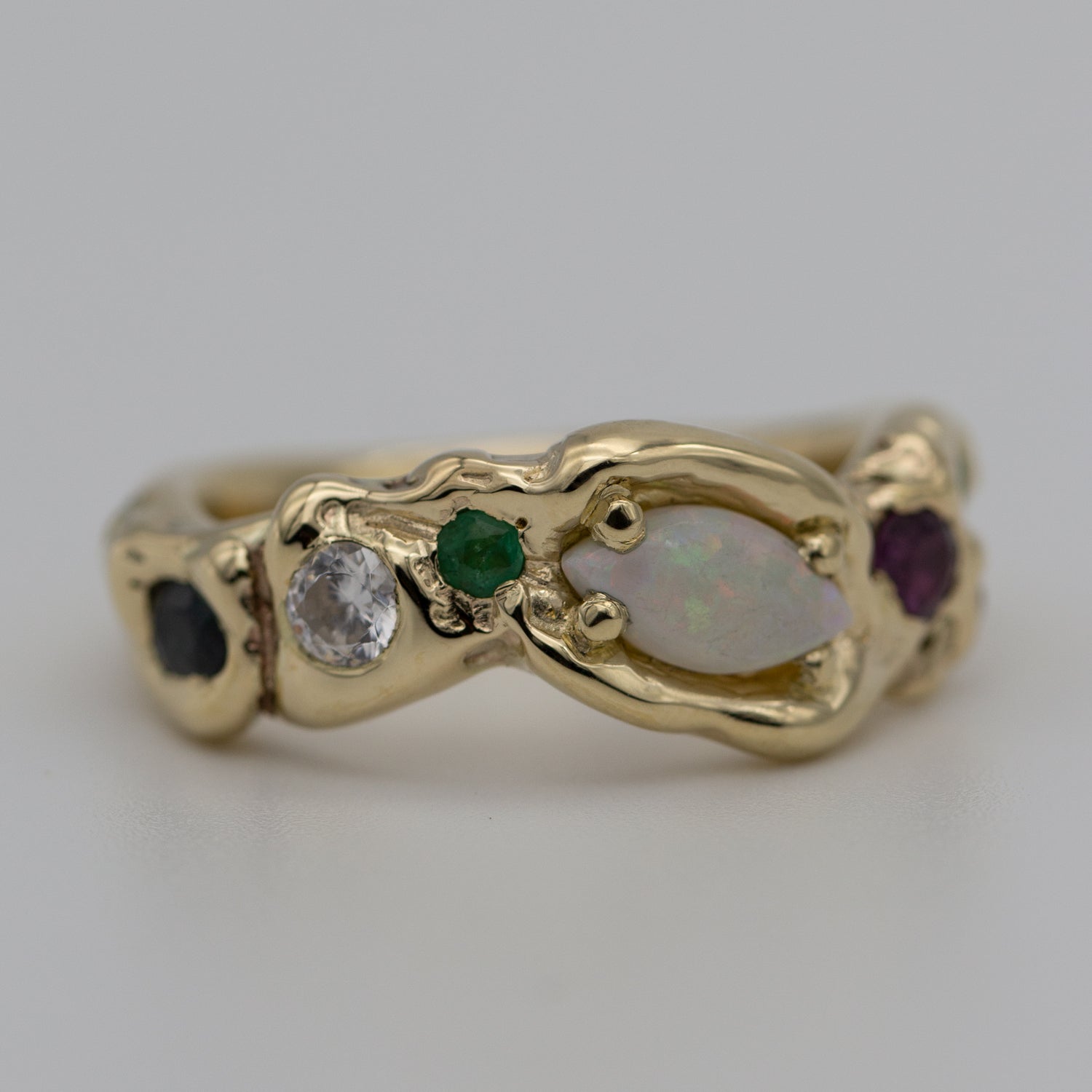 En unik formgivet ring i guld med Opal, diamant, smaragd, rubin ligger på hvid underlag. En unika ring i genanvendt 14kt guld