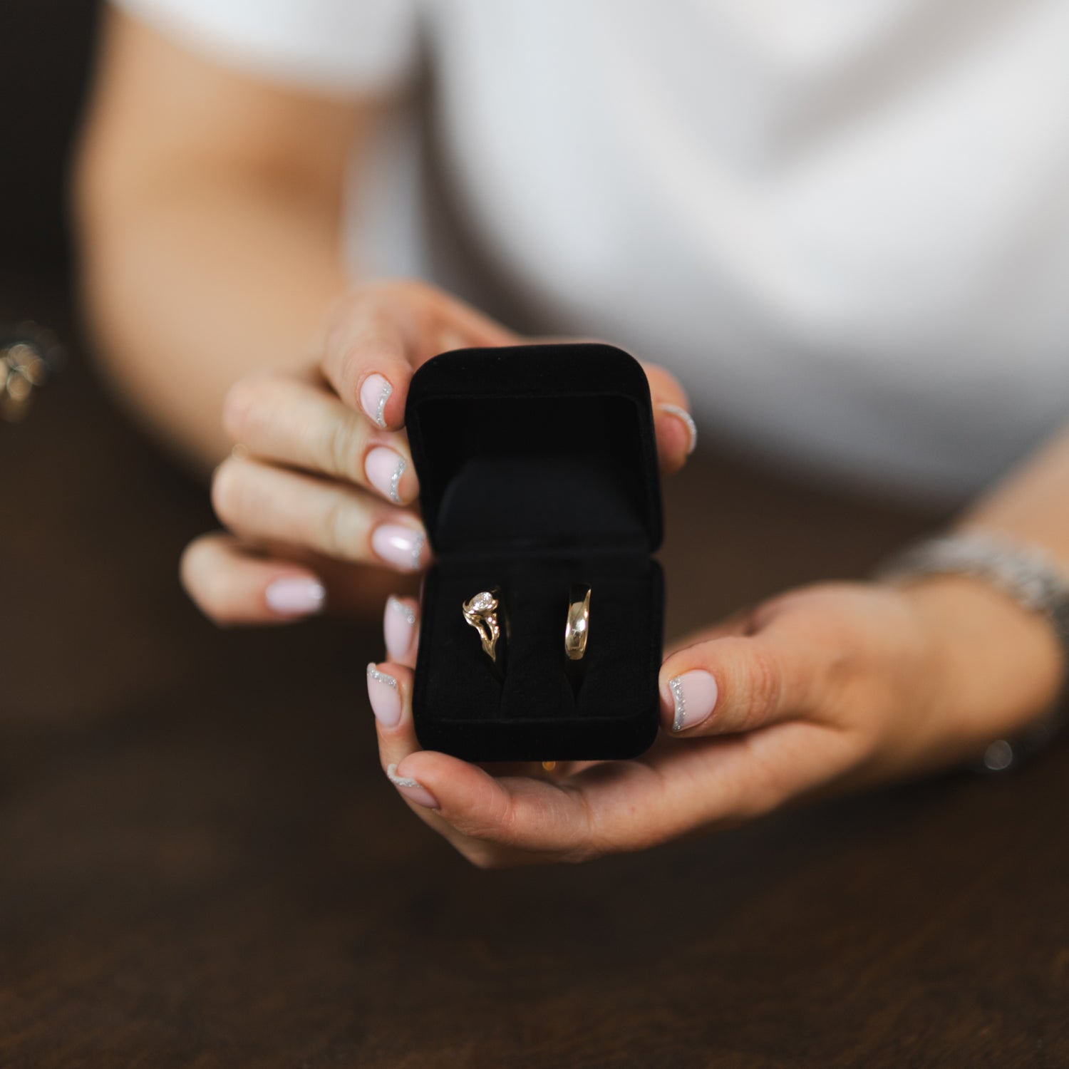 Michell Liljefelt holder et sæt vielsesringe i guld med organisk formgivning. Ringene sidder i en sort velour smykkeæske.