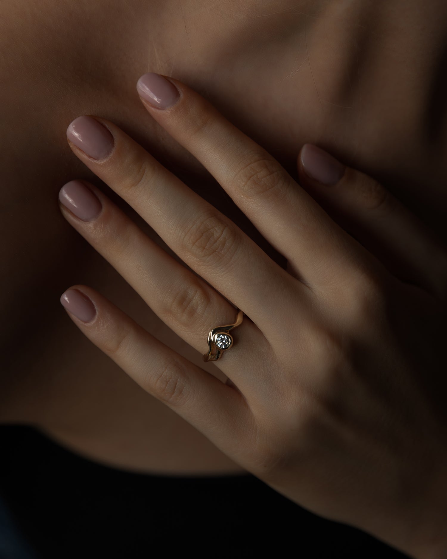 flot model hånd med diamant ring i guld. hånden holder på brystkassen, med sort top.  