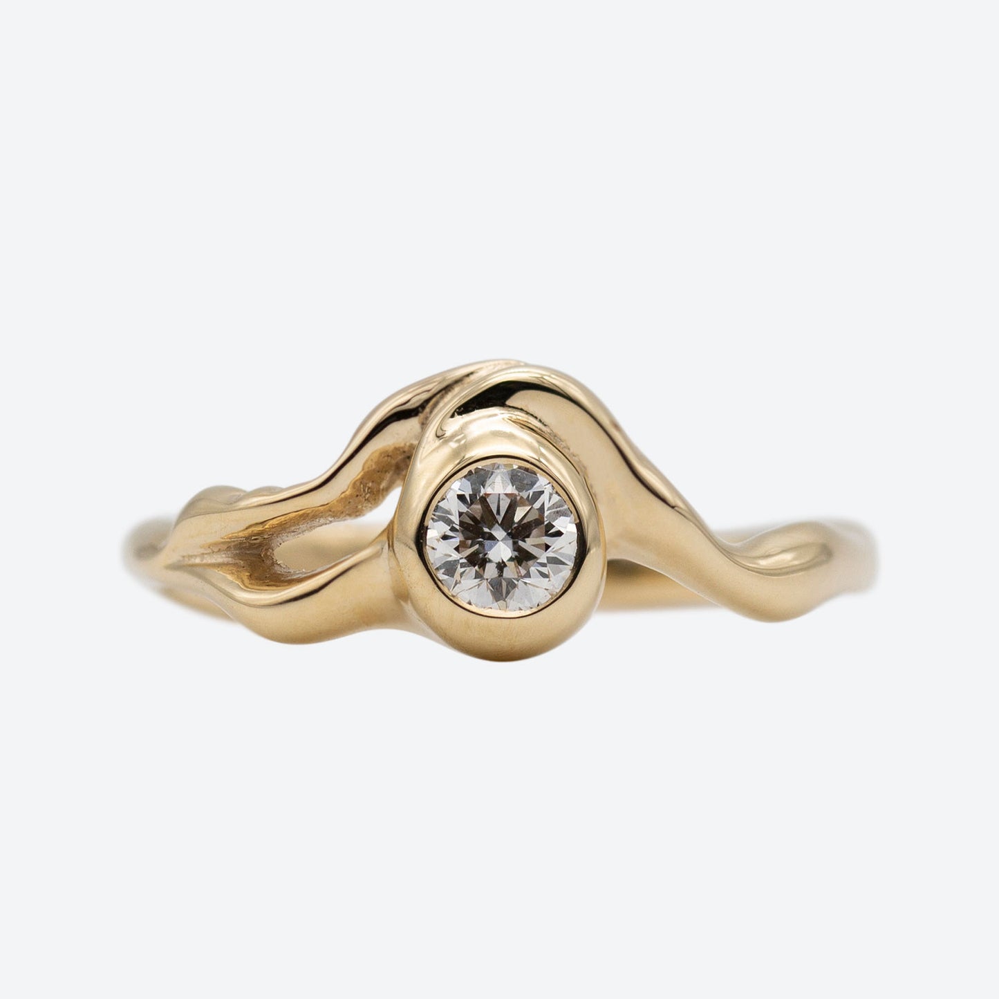 Organisk formgivet ring i guld med stor diamant placeret i centrum af ringen på hvid baggrund. Ud fra diamanten forgrener formgivningen sig rundt i ring skiven. Set forfra. 