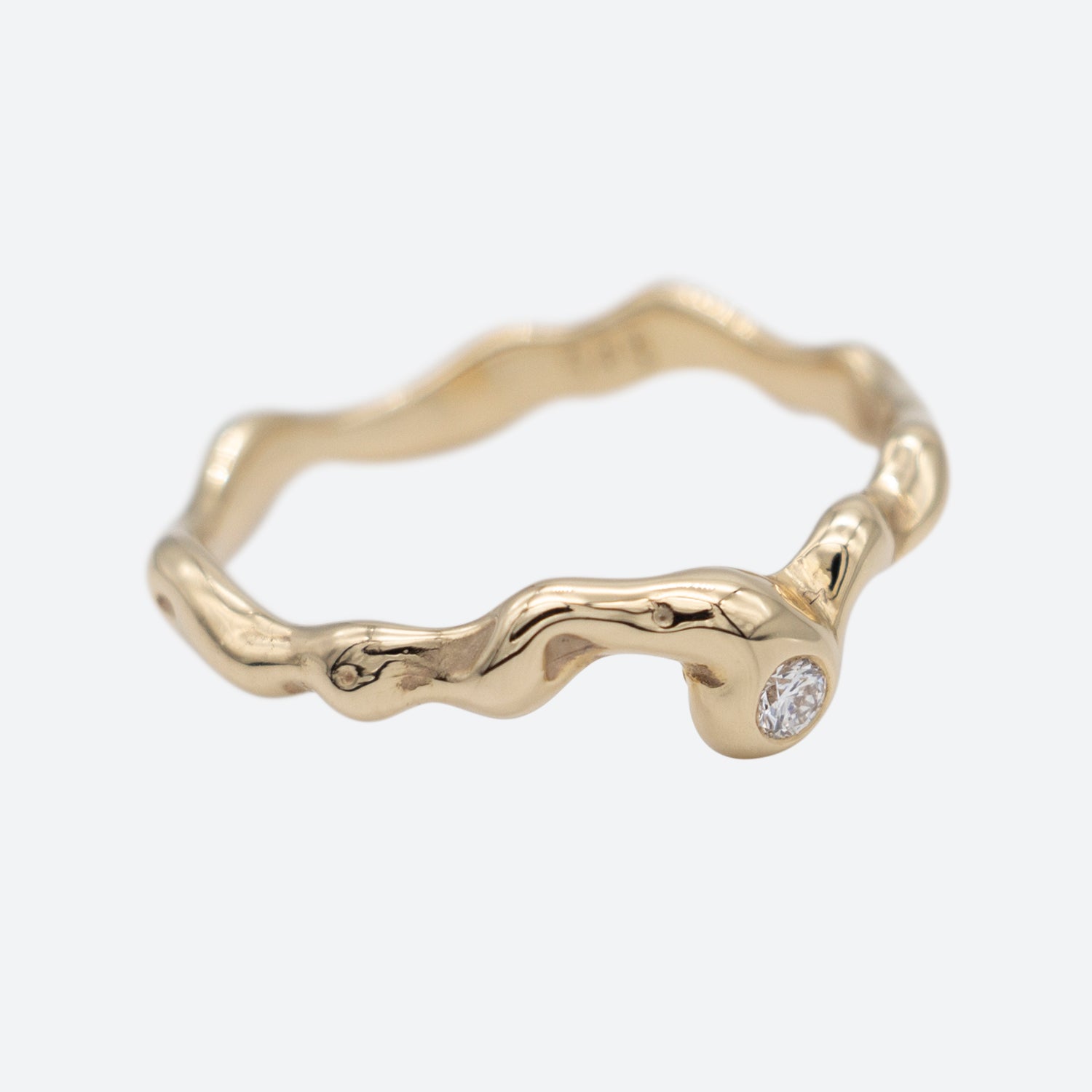 Organisk design ring i guld med en diamant på hvid baggrund. Design af Michell Liljefelt