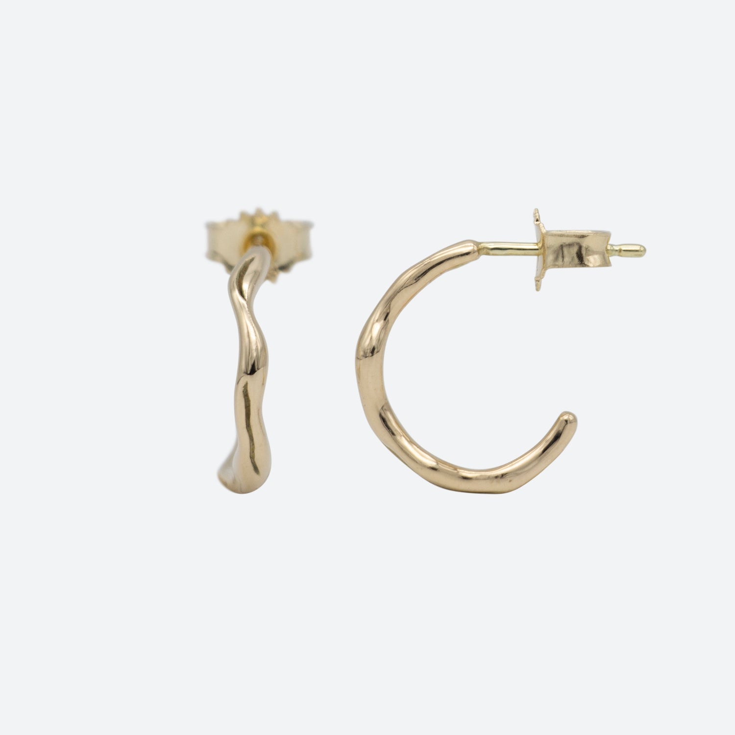To øreringe hoops i guld på hvid baggrund hvor den ene er med front og den anden med siden til. Begge er formgivet som creoler og med lås i guld. Design af Michell Liljefelt