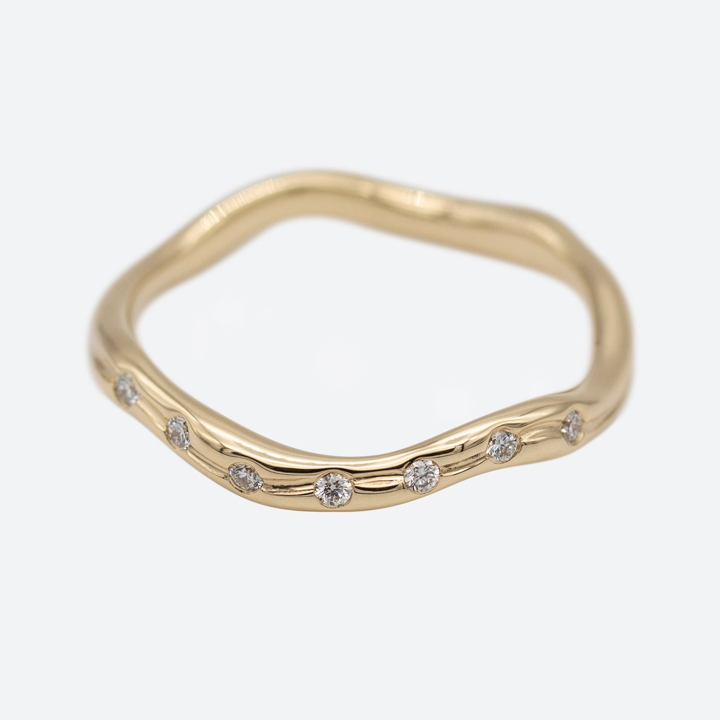 En ring i guld set i perspektiv med syv diamanter på hvid baggrund. Ringen er formgivet organisk og bølger elegant.