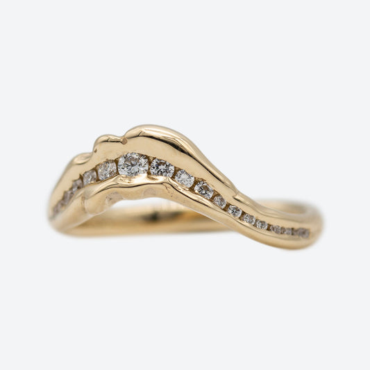 Ring i guld formgivet organisk set forfra med mange diamanter i et forløb der bugter sig som en bakketop. I midten er diamanterne størst og bliver mindre ud i mod siderne. Ringen er på hvid baggrund. 