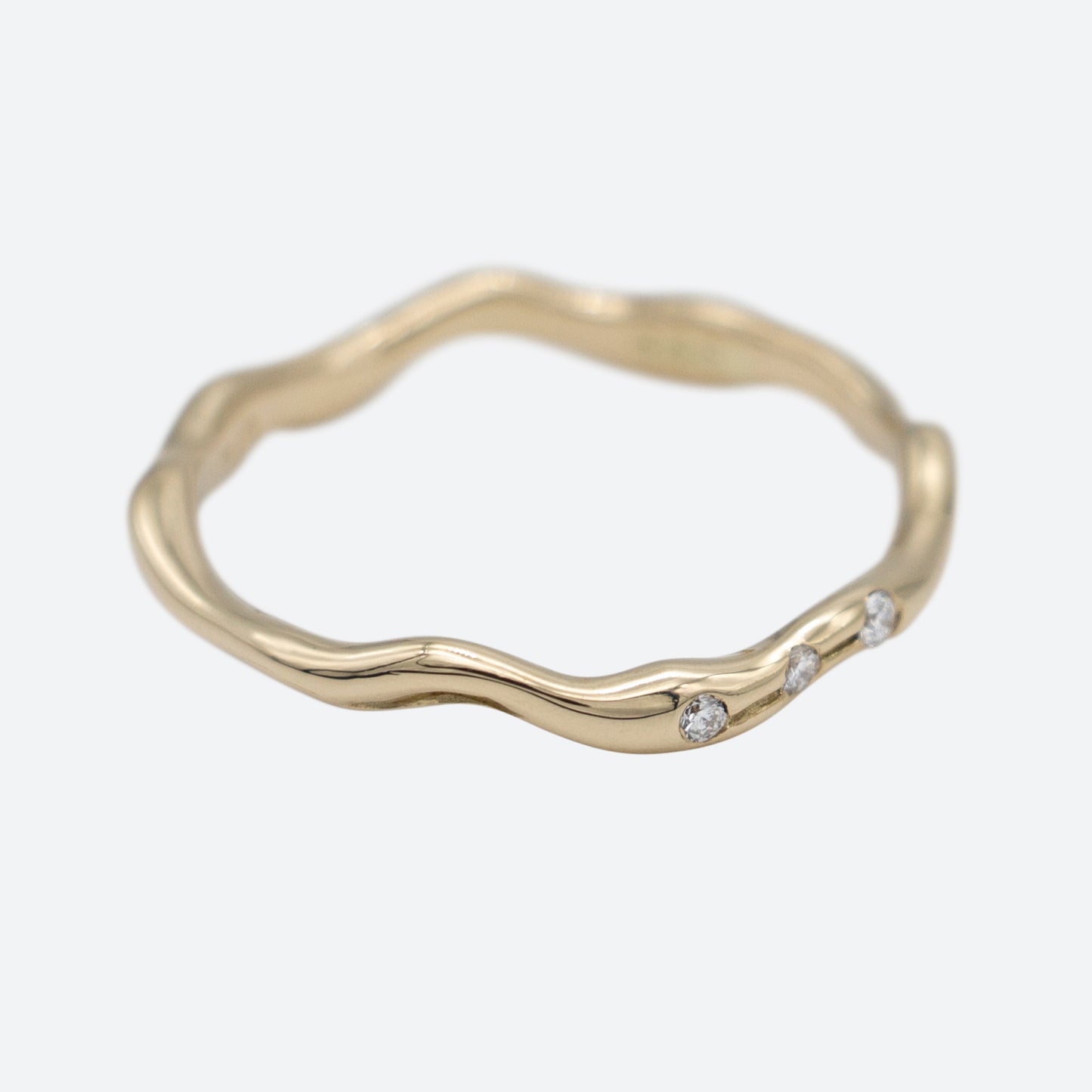 Smal ring i guld med tre diamanter på hvid baggrund set i perspektiv. Design af Michell Liljefelt