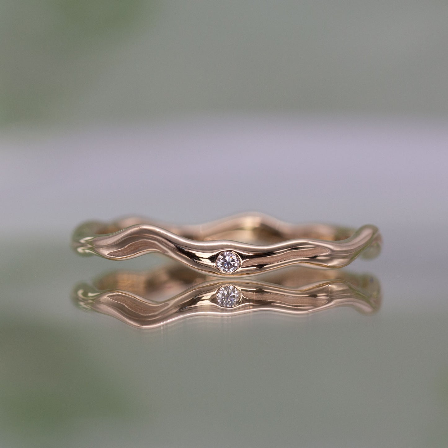 En tynd guld ring set forfra med en diamant. Formgivningen bugter sig i en harmonisk cirkel. 