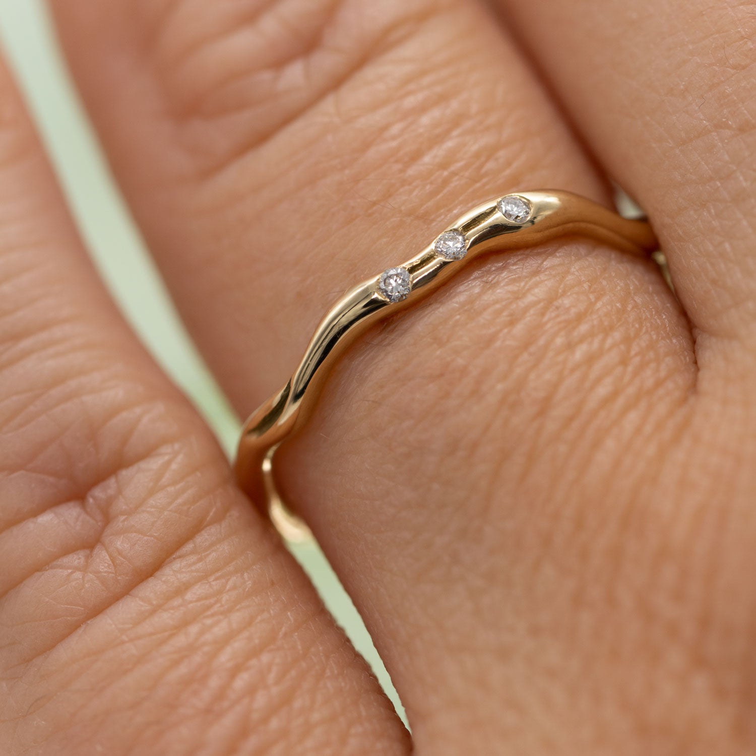 Closeup af udsnit af hånd med ring i guld centreret. Ringen har tre fairtrade diamanter og er organisk formgivet. 