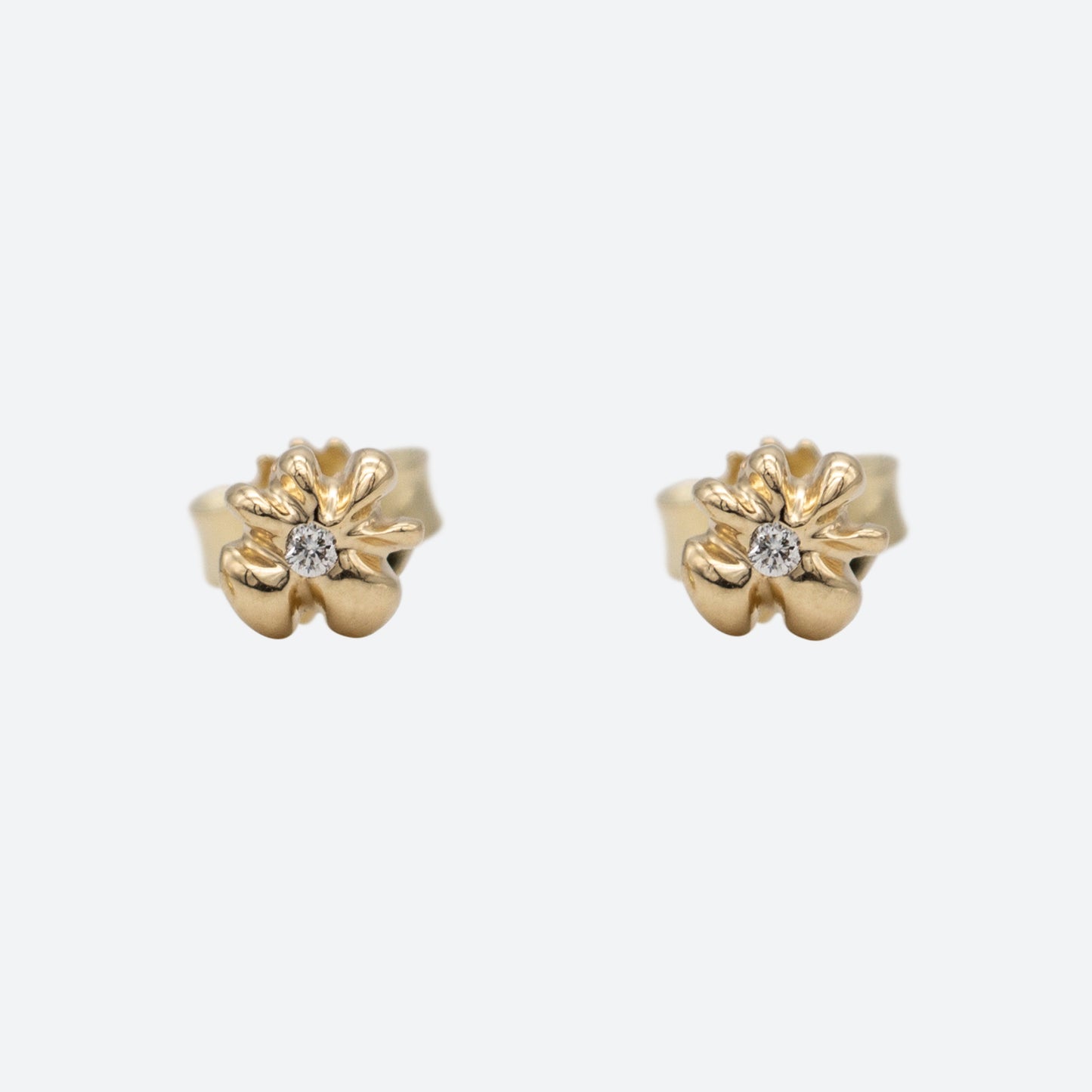To ørestikker i guld formet som en blomst med en diamant i midten set forfra på hvid baggrund. Design af Michell Liljefelt