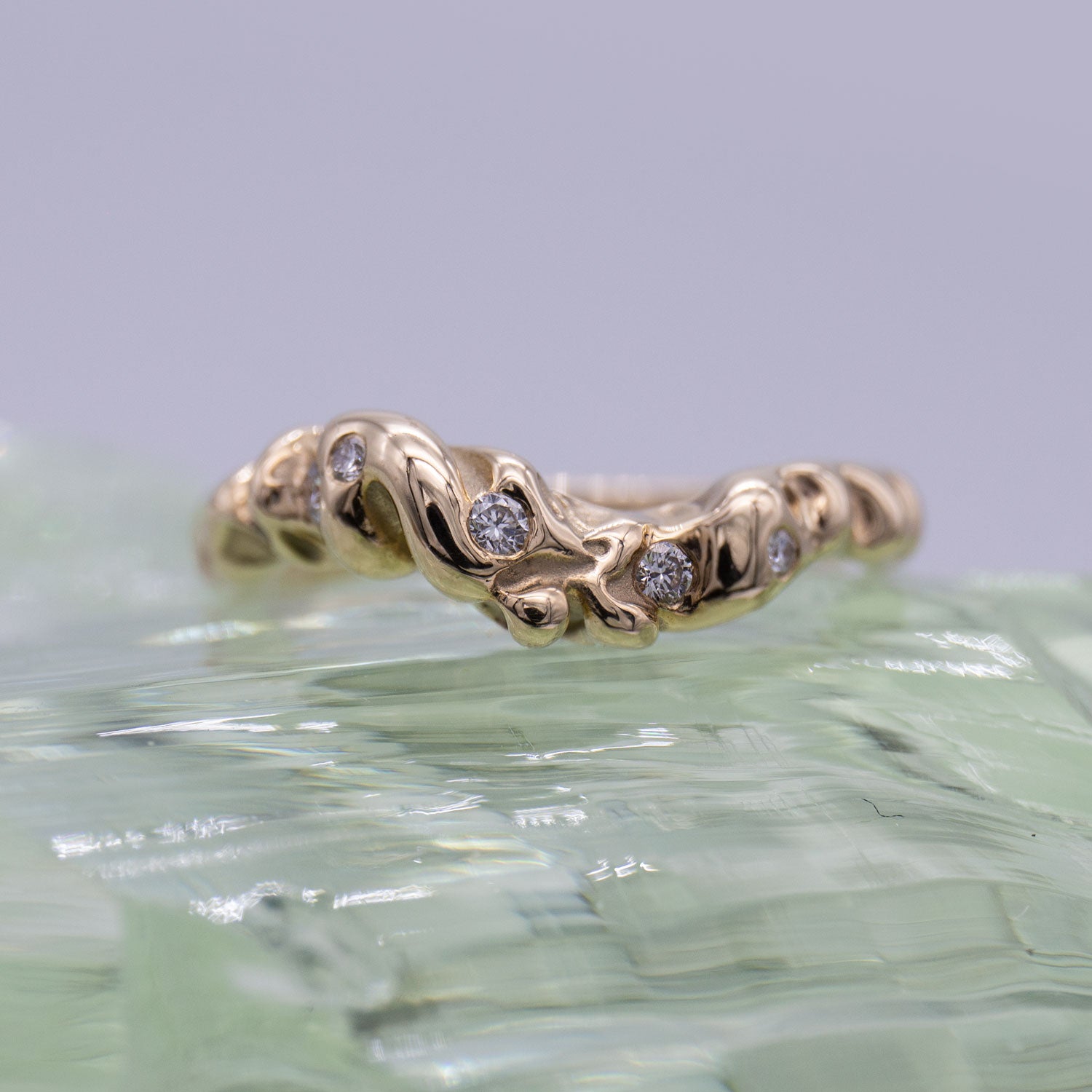 Ring i guld med fem diamanter ligger på en klump grønt glas.  Design af Michell Liljefelt