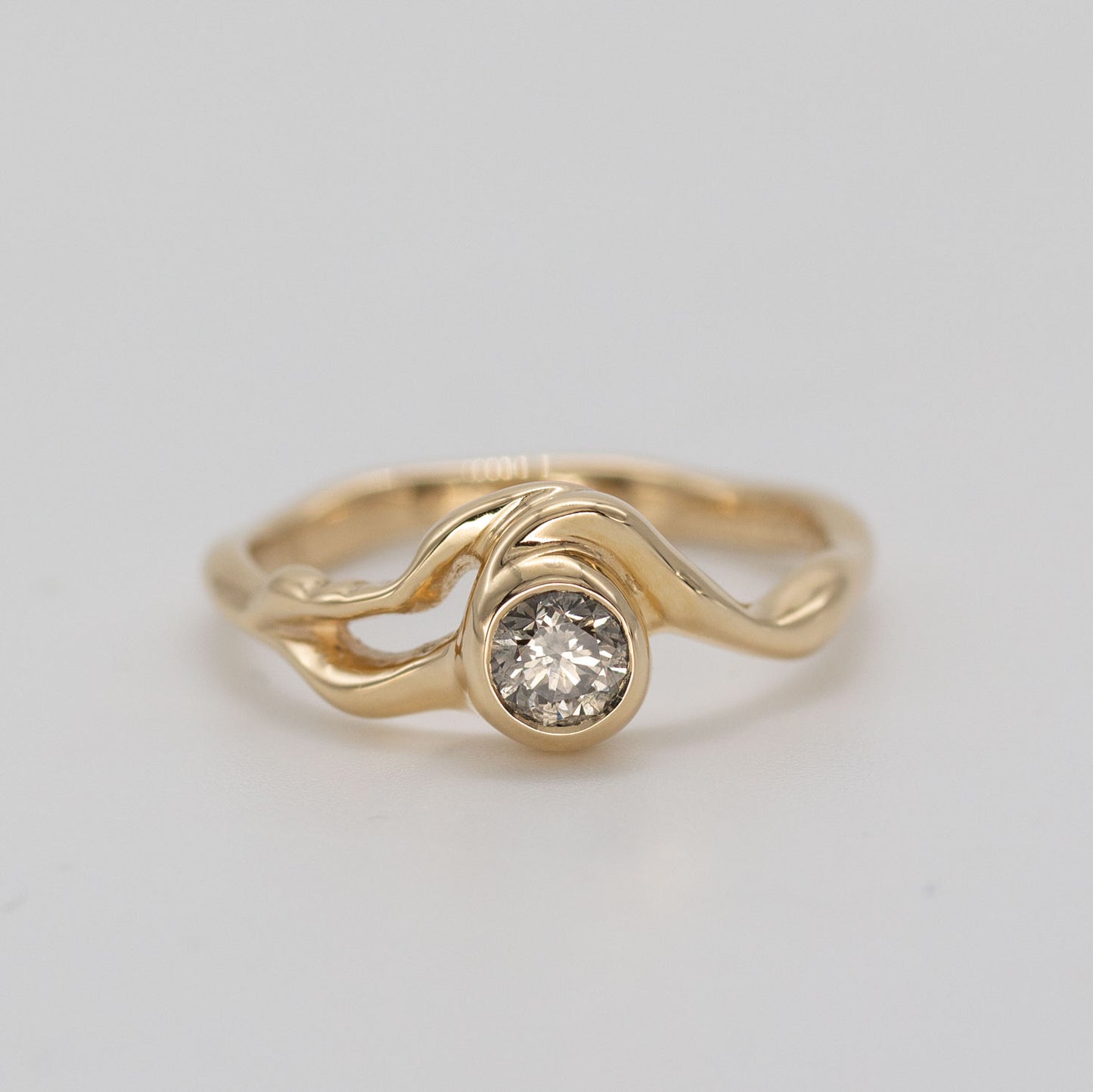 Organisk formgivet ring i guld med stor champagnefarvet diamant placeret i centrum af ringen på grå baggrund. Ud fra diamanten forgrener formgivningen sig rundt i ring skiven. Set forfra.