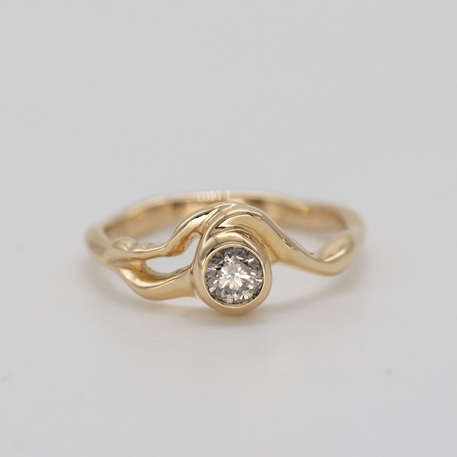 Organisk formgivet ring i guld med stor champagnefarvet diamant placeret i centrum af ringen på grå baggrund. Ud fra diamanten forgrener formgivningen sig rundt i ring skiven. Set forfra.