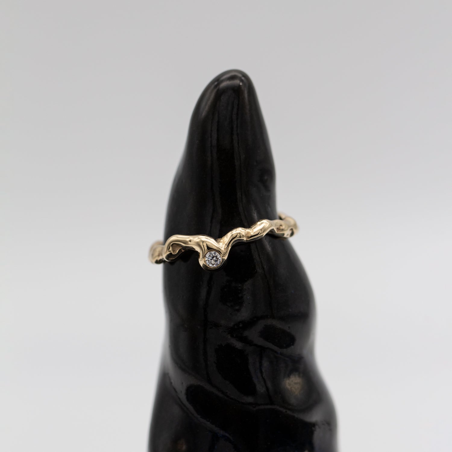 Organisk design ring i guld med en diamant på keramisk statue med sort glasur og hvid baggrund.  